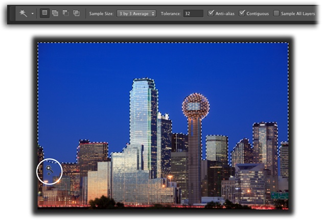 With its tolerance set to 32, the Magic Wand did a good job of selecting the sky behind downtown Dallas.You’ve got several ways to select the spots it missed, like the area circled at bottom left: You can add to the selection by pressing the Shift key while you click that area; increase the tool’s Tolerance setting, and then click the sky again to create a brand-new selection; or flip to page 164 to learn how to expand the selection with the Grow and Similar commands.