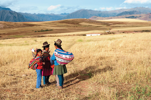 Photo showing three women standing on a grassland against mountain backdrop.